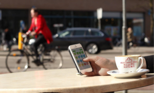 Hand counting cyclist using Counterpoint app on phone with a coffee cup in front with the Velo Canada Bikes Logo